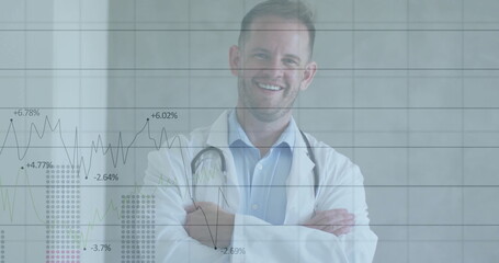Standing doctor crossing arms smiling in medical corridor, with lab coat, stethoscope and charts