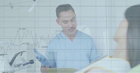 Consulting dentist in blue scrubs reviewing chart with patient in treatment room