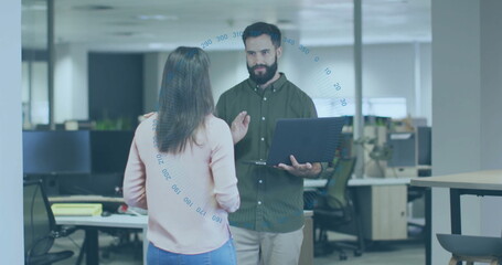 Obraz premium Holding laptop, coworkers wearing business attire discussing project in open plan office