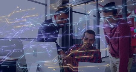 Pointing and typing colleagues reviewing code on laptop and monitor in office, with circuit overlay