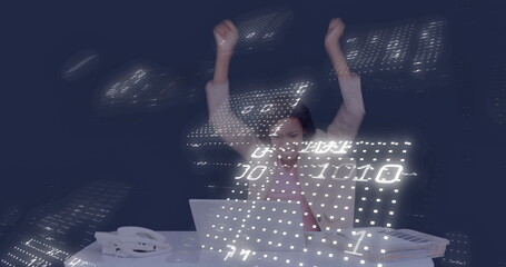 Cheering female data analyst raising arms at office desk, with laptop and binary code overlays