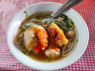 Meatball. A bowl of meatballs complete with yellow noodles, crispy fried dumplings, etc., served with delicious thick sauce on the table.