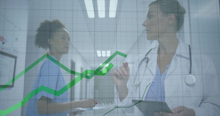 Doctor wearing white coat pointing at glass charts holding tablet in hospital corridor, copy space