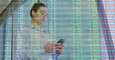 Examining floating market data, business professional holding smartphone in lobby with glass wall