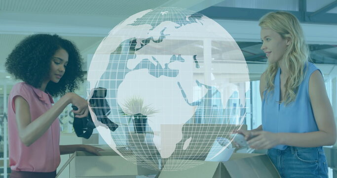 Two women sorting boxes and examining wireless headphones at office counter, with globe graphic - Powered by Adobe