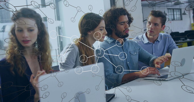Office workers in business attire collaborating at desk with laptops and network overlay in office
