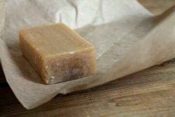 A piece of natural laundry soap on craft paper, on a wooden background, close-up.