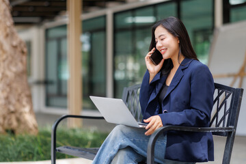 Businesswoman working remotely using laptop and talking on phone outdoors