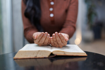 Woman praying with open hands over holy book on table