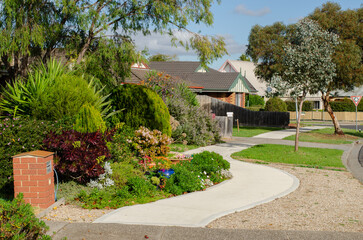 Obraz premium A curved concrete footpath along the front garden in a suburban neighborhood in Australia. Well-maintained yard in a welcoming residential street.