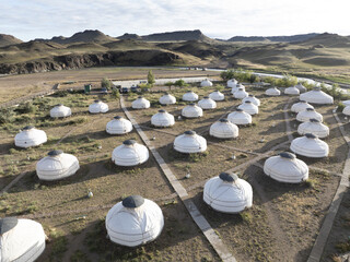 Aerial view of a cluster of traditional yurts dot the arid landscape, nestled near rolling hills and a winding river, Turgen, Uvs, Mongolia.