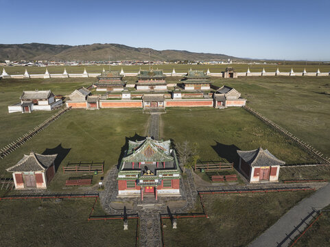 Aerial view of vibrant temples with red and green roofs stand in stark contrast to the expansive, grassy plains under a clear sky, Turgen, Uvs, Mongolia.