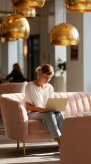 Obraz premium Young woman working on a laptop in a modern cafe with stylish golden accents in the afternoon