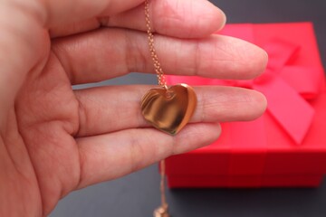 Fototapeta premium Woman's hand holding a heart shaped necklace presented as a gift in a red box.