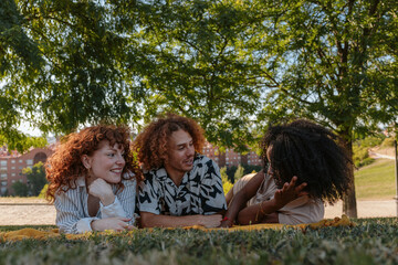 Friends enjoying summer holidays lying on grass in a park talking and smiling