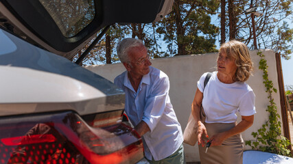 Senior couple loading luggage into car trunk before road trip