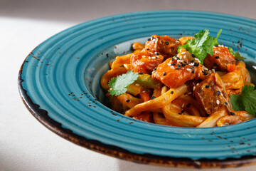 Korean stir fried udon noodles with grilled salmon cubes, vegetables, sesame seeds and herbs served...