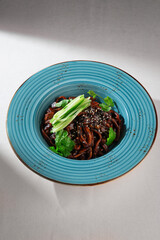Traditional Korean jajangmyeon noodles with rich black bean sauce, fresh cucumber, sesame seeds and herbs served in a rustic blue ceramic bowl