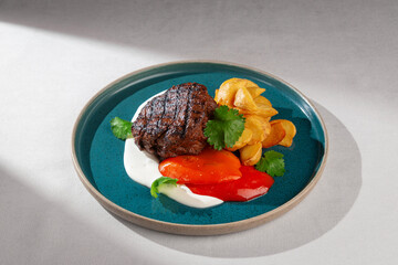 Juicy grilled beef steak with golden roasted potatoes, red sweet pepper, creamy white sauce and...