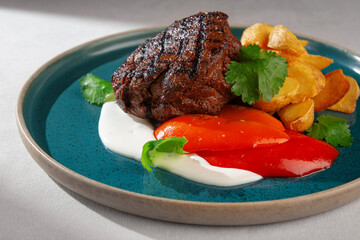 Juicy grilled beef steak with golden roasted potatoes, red sweet pepper, creamy white sauce and...
