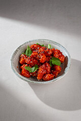 Korean yangnyeom chicken with crispy coating, tossed in sweet and spicy red sauce, garnished with...