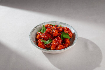 Korean yangnyeom chicken with crispy coating, tossed in sweet and spicy red sauce, garnished with...