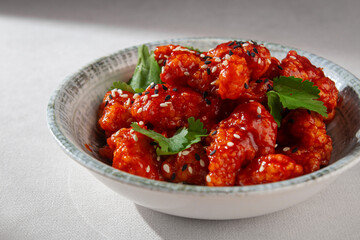 Korean yangnyeom chicken with crispy coating, tossed in sweet and spicy red sauce, garnished with...