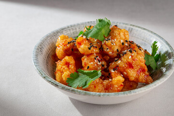 Crispy Korean chicken bites coated in glossy sweet chili sauce, sprinkled with sesame seeds and garnished with cilantro, served in a rustic ceramic bowl