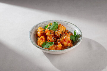 Crispy Korean chicken bites coated in glossy sweet chili sauce, sprinkled with sesame seeds and garnished with cilantro, served in a rustic ceramic bowl