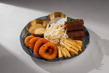A rich beer snack platter with crispy onion rings, golden French fries, cheese strings, toasted rye bread with dill and two sauces served on a blue ceramic plate