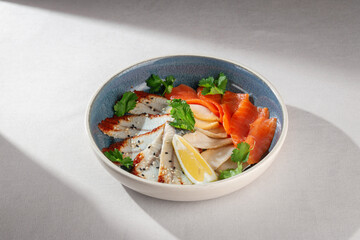 Gourmet selection of sliced seafood including smoked salmon, marinated fish fillet and calamari, garnished with sesame seeds, lemon wedge and fresh parsley in ceramic bowl