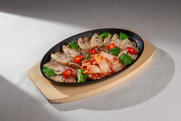 Sliced pork belly served on cast iron plate with traditional Korean kimchi, fresh cilantro, black sesame seeds and red chili peppers for garnish