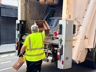 Caucasian male sanitation worker loading cardboard boxes into garbage truck