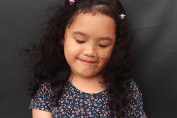 Asian girl with curly hair looks seriously at a toothless tooth in her hand, close up and dark...