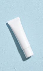 White cosmetic cream tube mockup on a light blue textured background. Skincare product packaging for beauty and wellness branding.