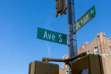 A street corner with clear blue skies above. Two green street signs are prominently displayed on a utility pole, indicating