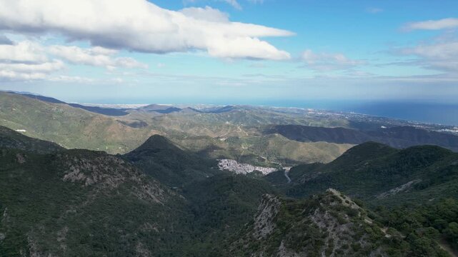 Aerial view of the Ojen town nestled between lush green mountains under a partly cloudy sky, a contrast of nature's beauty, Ojen, Marbella, Spain.