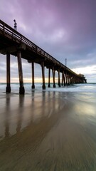 Obraz premium Long wooden pier extending into ocean at sunset, reflecting in wet sand