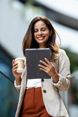 Fototapeta premium Smiling businesswoman using digital tablet and holding coffee outside office building