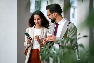 Business colleagues enjoying coffee and discussing work on smartphone