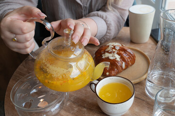 A woman is gently pouring tea into a cup that is situated on a table