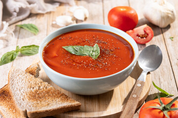 Homemade Tomato Soup in bowl with Basil on rustic wooden table