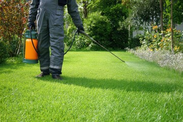 Worker applies pest control spray on lush green lawn in a residential garden during daylight hours for effective pest management