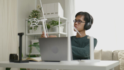 Asian male designer sitting and inspecting his 3D printed creation made from recycled materials.