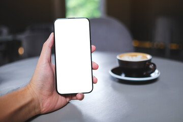 Mockup image of a man holding mobile phone with blank white screen in cafe