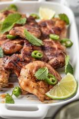 Spicy grilled chicken thighs roasted with chilli and lime on white dish close up, light gray kitchen background