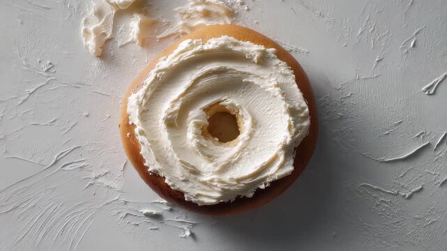 Overhead camera rotating around bagel with smooth cream cheese spread on top, minimal white background, slow cinematic motion, modern food concept, stylish breakfast video loop
