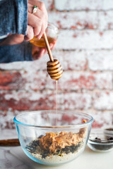 Honey dipper with honey dripping from it into a bowl as a woman prepares homemade energy bites. 