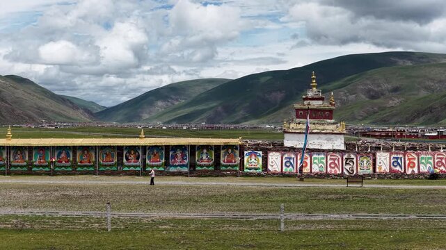 Aerial view of the Bage Mani Stone Wall, where colorful murals and Tibetan scripts contrast against the backdrop of green hills, Bage, Sichuan, China.