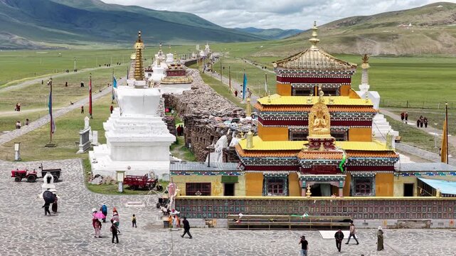 Aerial view of the golden-roofed buildings and white stupas along the Bage Mani Stone Wall, contrasting with the green grassland, Bage, Sichuan, China.